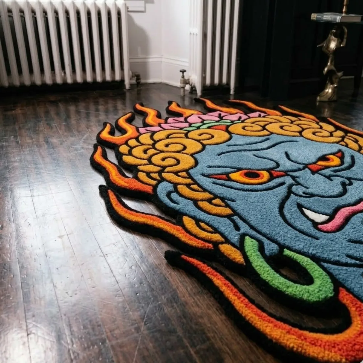 A low-angle view of the Fudo Myoo rug placed on a dark wood floor in a beautifully lit room setting. This highly detailed, 8k quality shot highlights the crisp color blocking of the traditional Japanese tattoo design, emphasizing the textured flames and striking facial features. The thick tufted yarn is built with internal stuffing for a luxurious, natural softness, perfectly capturing the bold, unshaded style of this custom-shaped piece.
