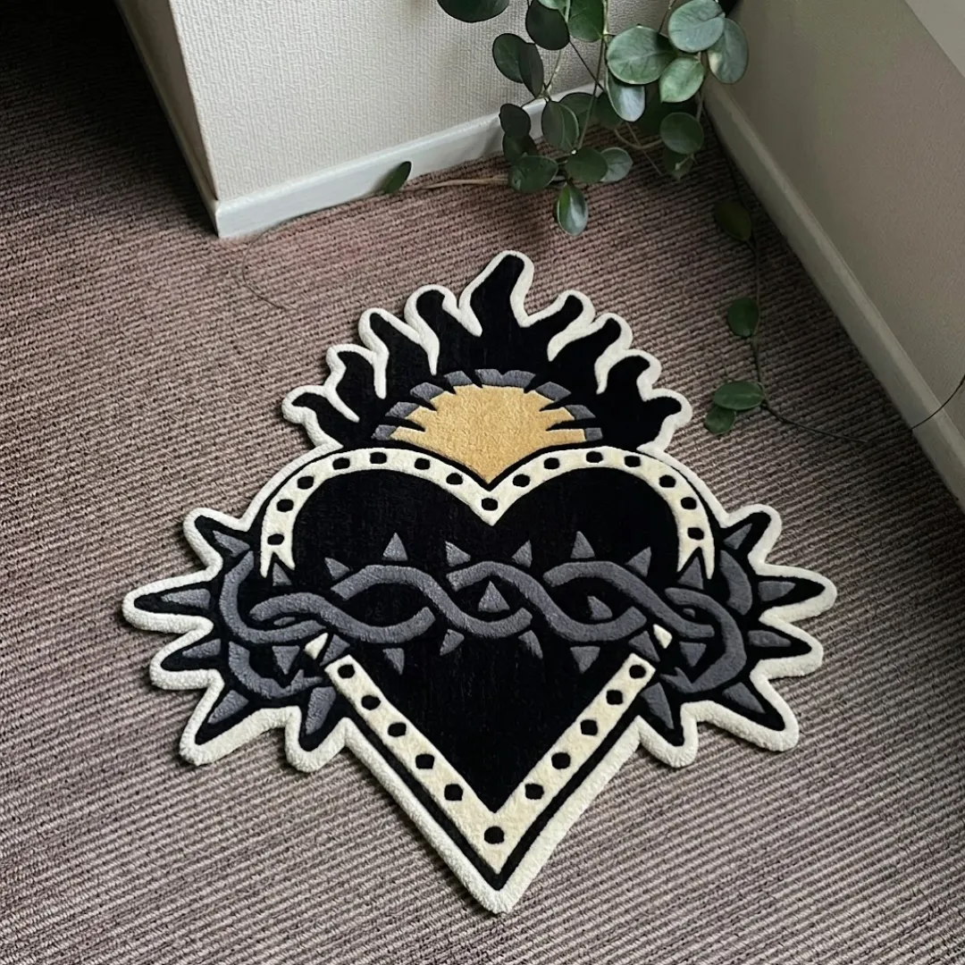 Sacred Heart traditional tattoo style heart shaped tufted area rug with flames and crown of thorns, displayed flat on a textured carpeted floor.