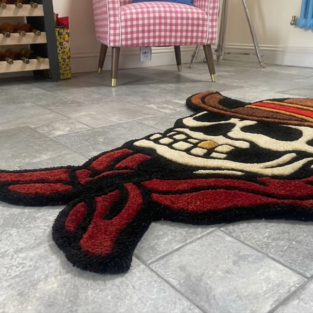 skull cowboy traditional rug close up A low-angle, extreme close-up of the Skull Cowboy rug resting on a grey tiled floor. The detailed shot highlights the thick, plush tufted yarn texture of the red bandana and the skull's teeth, emphasizing the crisp lines of the American traditional tattoo aesthetic, with a pink checkered chair softly blurred in the background.