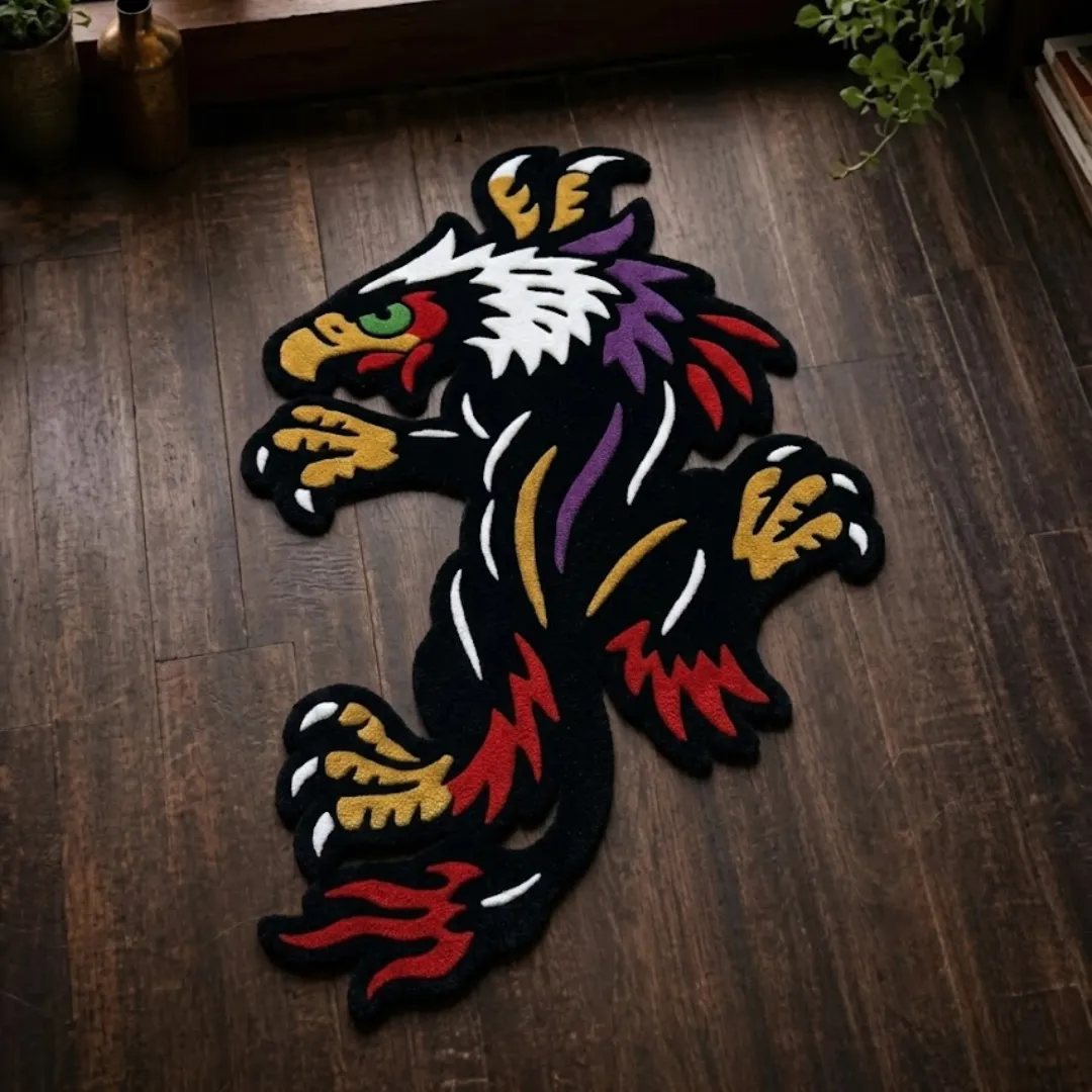 A top-down studio product photograph of a unique, eagle-shaped area rug featuring a black crawling eagle design with vibrant red, yellow, and purple accents, displayed on a dark wooden floor.