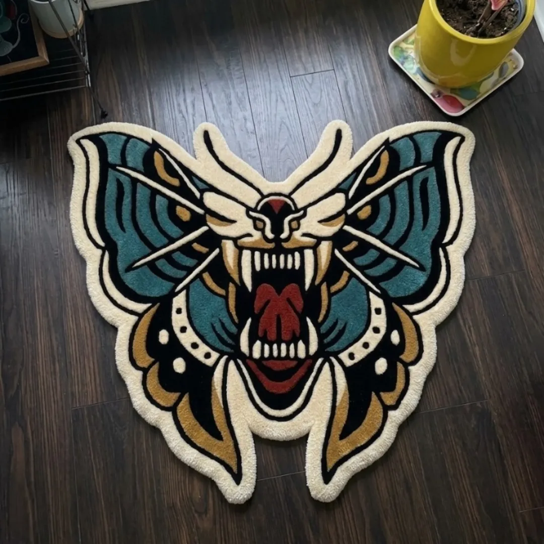 A top-down studio product photograph of a unique, moth-shaped area rug featuring a roaring feline face motif in vibrant teal, red, and gold, displayed on dark wood flooring.