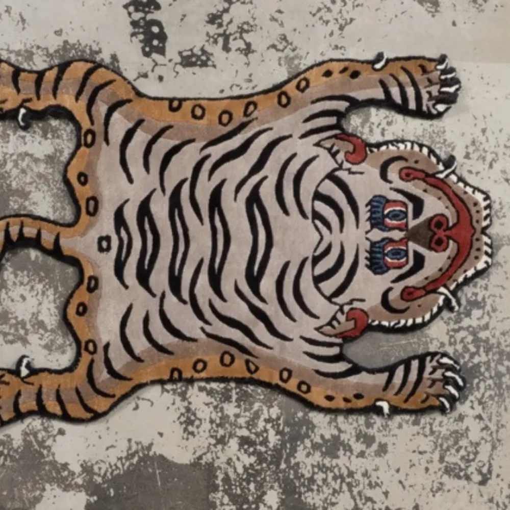 Hand tufted brown Tibetan-style tiger rug with black stripes, red face details, and a playful smile, placed on a concrete textured floor.