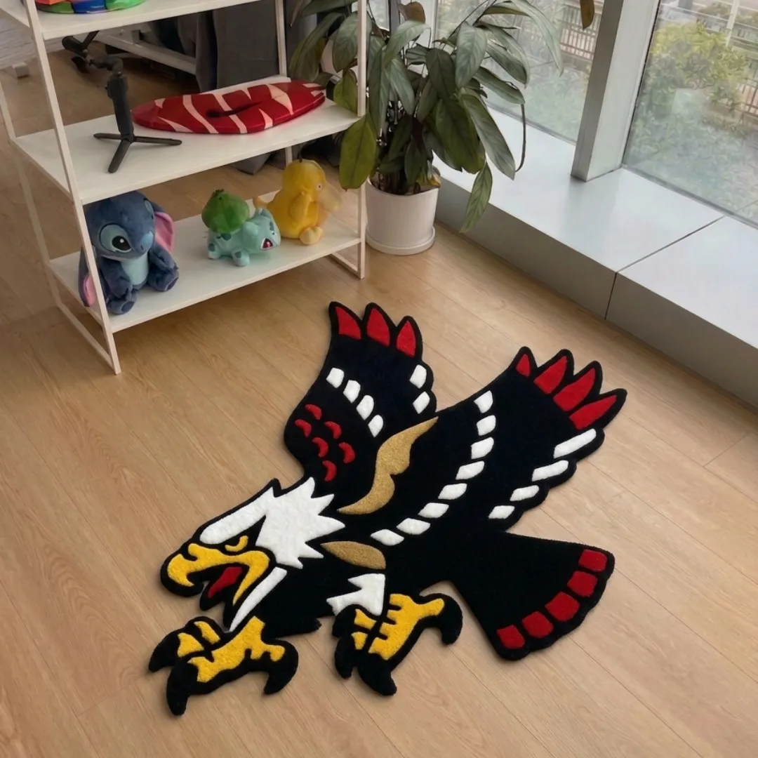 A top-down studio product photograph of a unique, eagle-shaped area rug featuring a black, white, red, and yellow design styled on light wooden flooring.