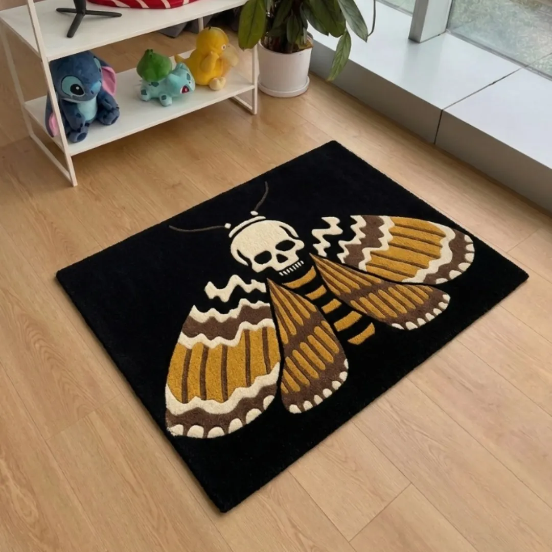 An interior view of a dark gothic-themed area rug featuring a skull moth design, placed on light wood flooring in a room with a white storage shelf featuring character collectibles.