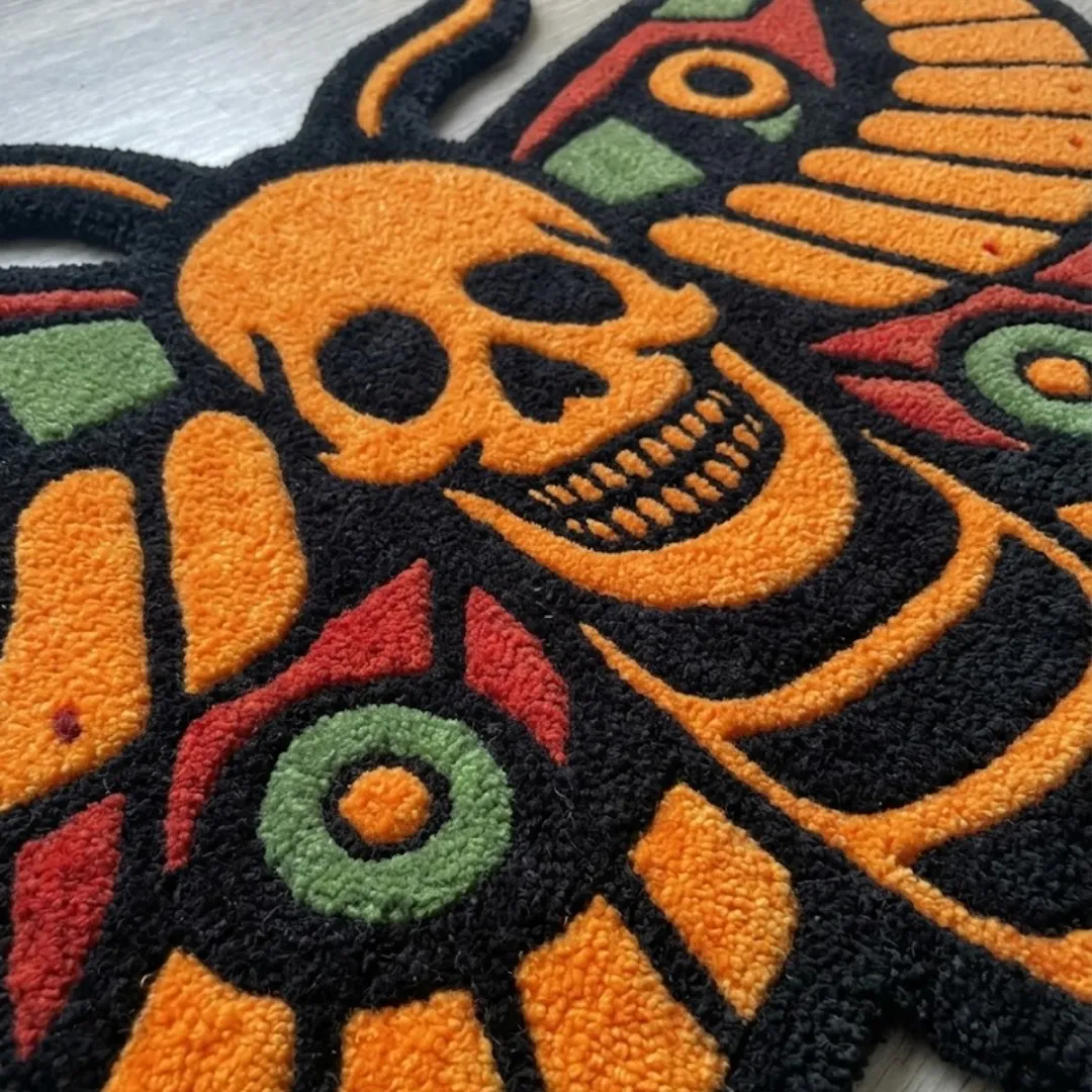 A macro close-up of the orange death head moth rug, focusing on the dense, tufted wool pile and the intricate graphic design of the skull and moth wings.
