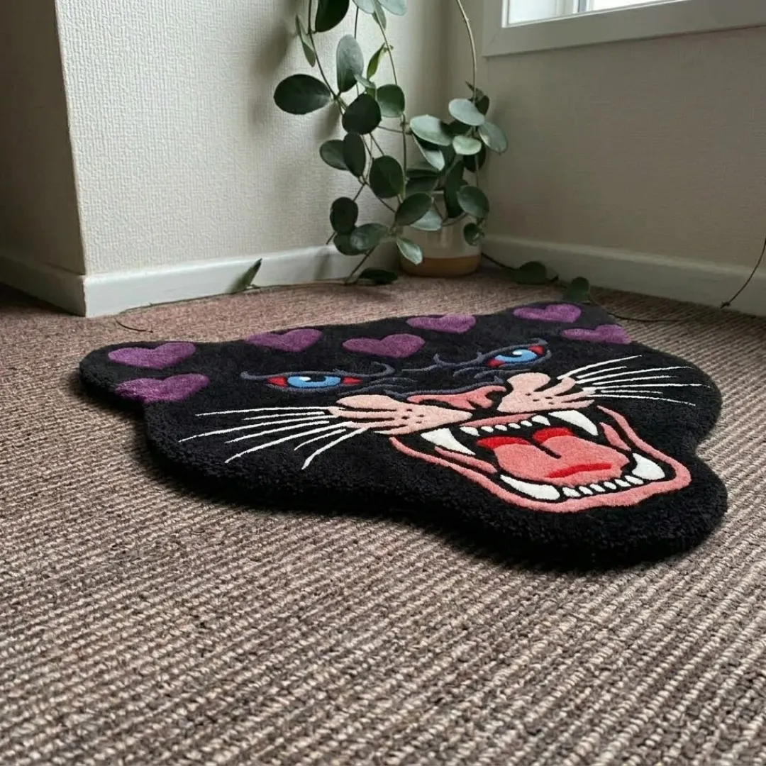 An angled perspective shot of a hand-tufted purple panther head rug, highlighting its expressive feline silhouette and high-quality tufted wool texture on a carpeted floor.