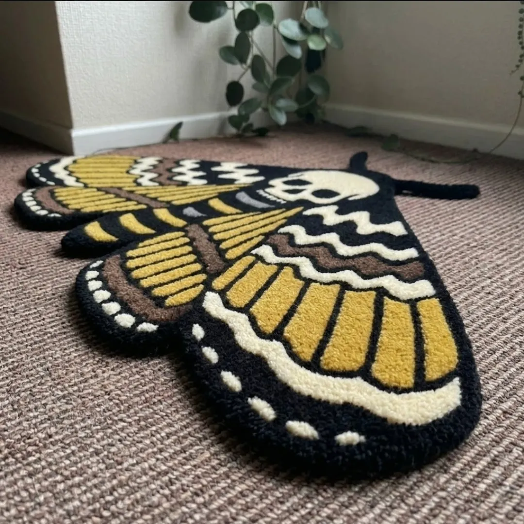 An angled perspective shot of a hand-tufted skull moth rug, highlighting its expressive moth silhouette and the high-quality wool texture on a carpeted floor.