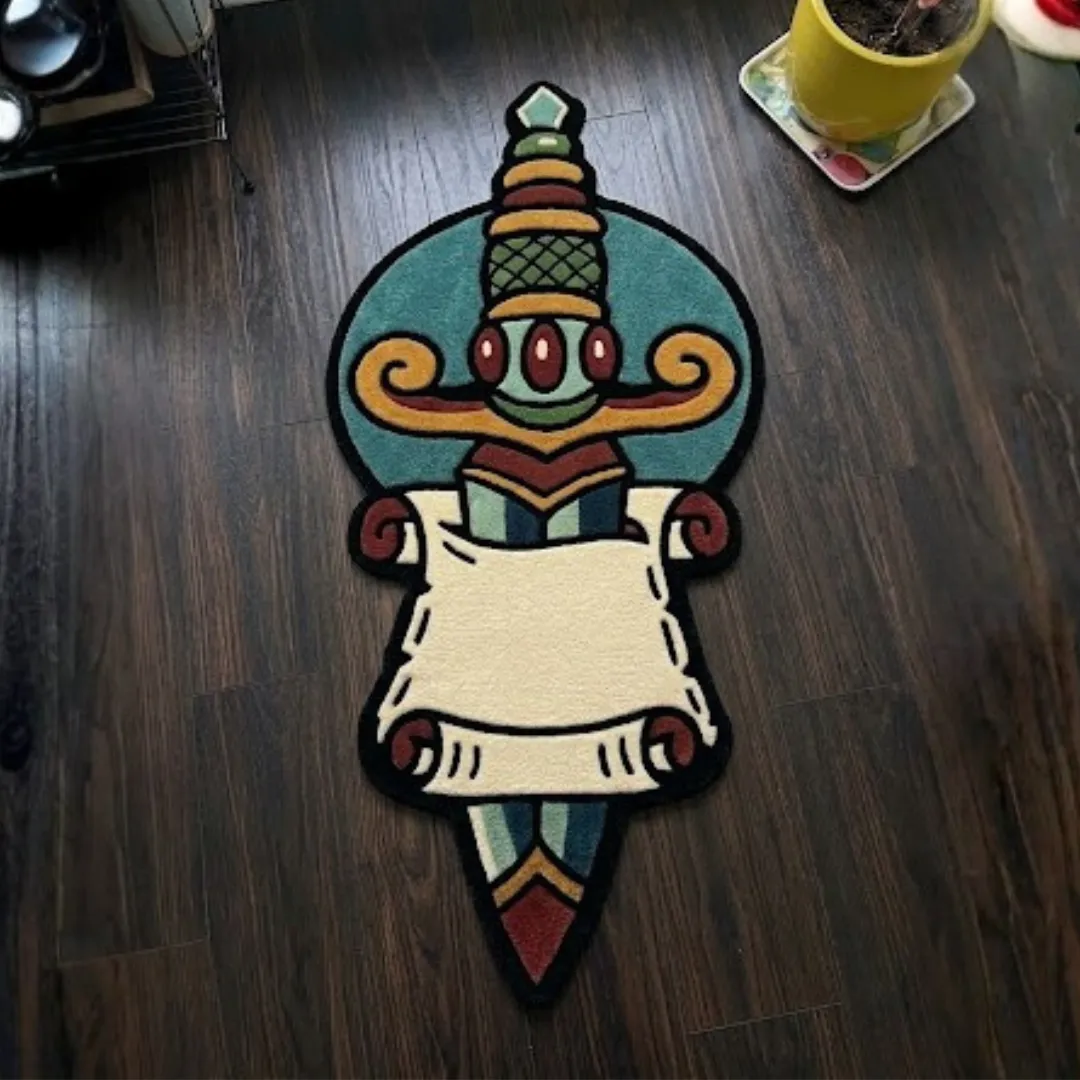 A top-down studio product photograph of a unique, dagger-shaped area rug featuring a traditional tattoo-style dagger piercing a blank scroll, displayed on a dark wooden floor.