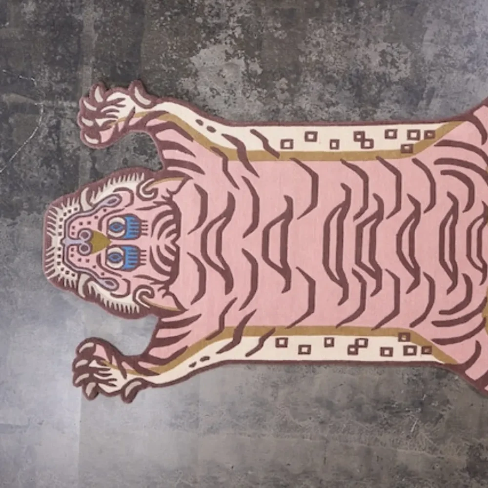 Cream and pink wool rug with tiger motif, inspired by Tibetan tiger skin rugs, placed on a stone floor.