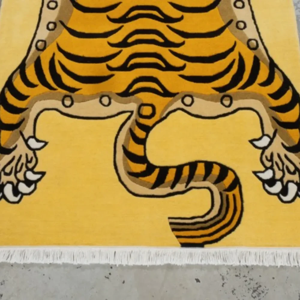 Yellow tiger rug with bold black stripes, red face details, and white fringe, displayed on a gray concrete floor.