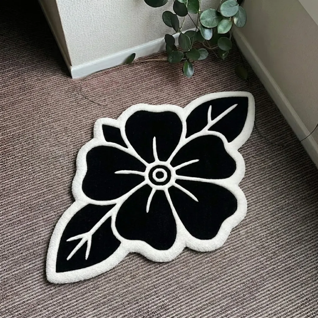 Blackwork Rose traditional tattoo style black and white floral shaped tufted area rug displayed flat on a textured carpeted floor.