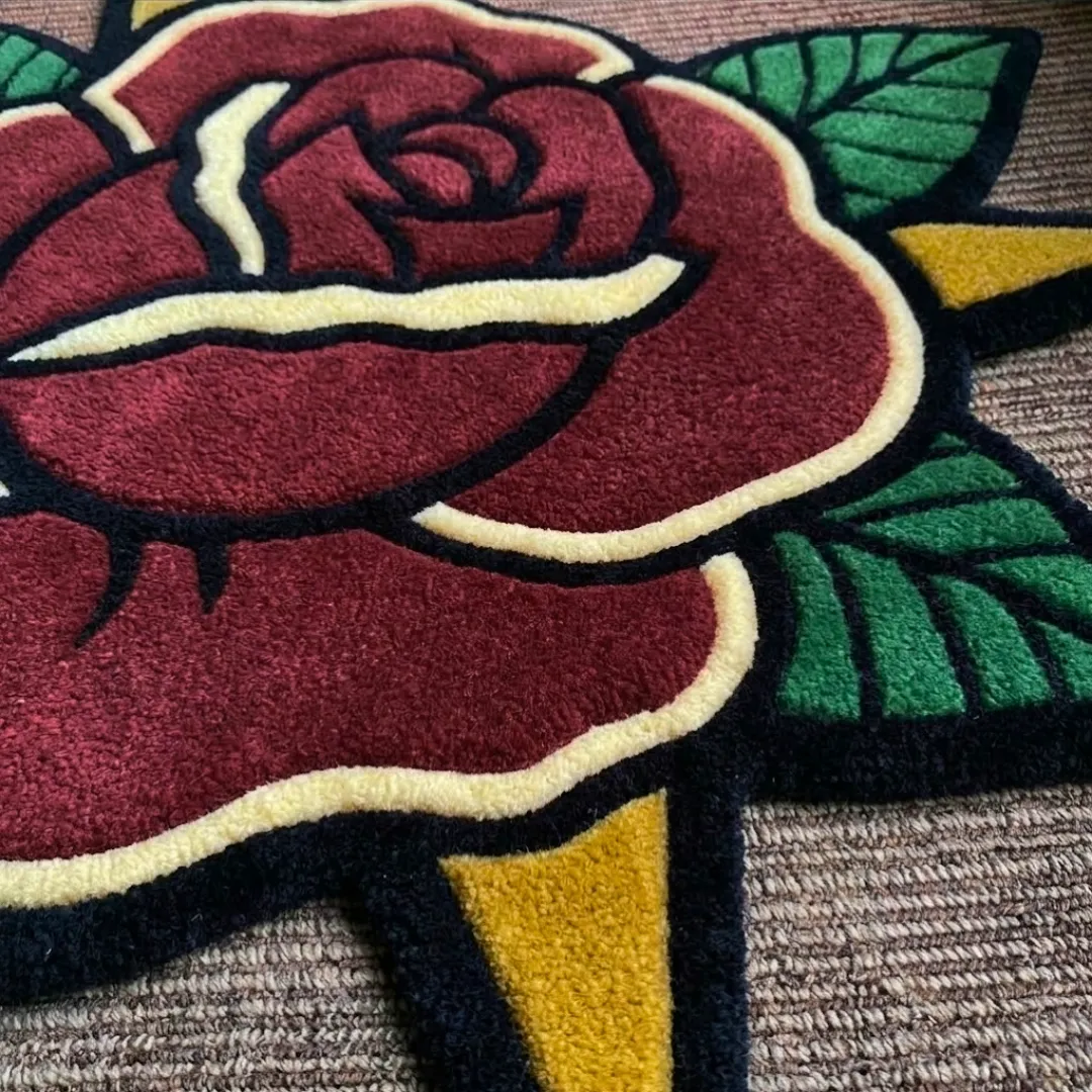 An interior lifestyle shot of a tattoo-inspired red rose area rug positioned in a room corner, showing its vibrant floral silhouette on a carpeted floor near a potted plant.
