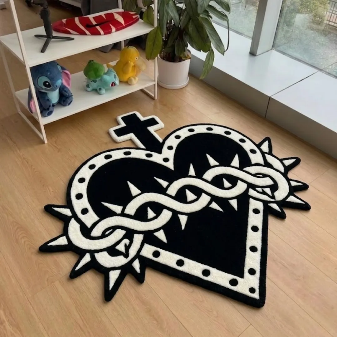 An interior lifestyle photograph of a black and white cross-heart area rug placed on a wooden floor in a styled room, near a shelf with character collectibles.