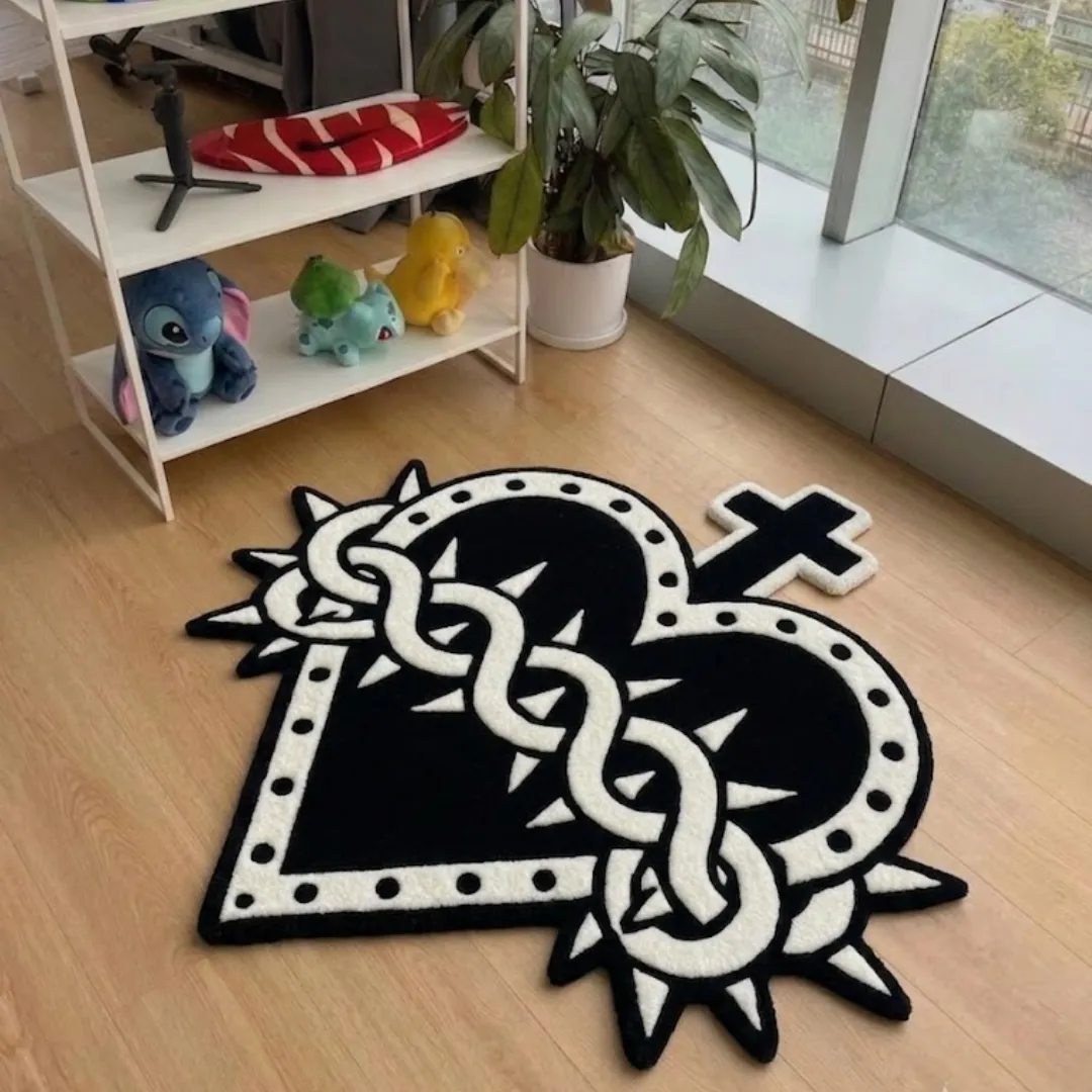 A top-down studio product photograph of a unique cross-and-heart-shaped area rug featuring high-contrast black and white gothic-inspired designs, displayed on hardwood flooring.