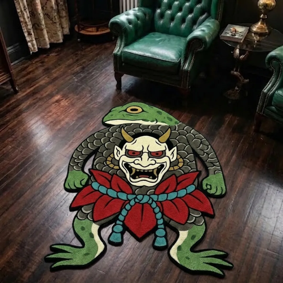 A top-down studio product photograph of a unique, frog-shaped area rug featuring a central Japanese-style oni demon mask, vibrant red floral details, and a blue rope design, displayed on a wooden floor.