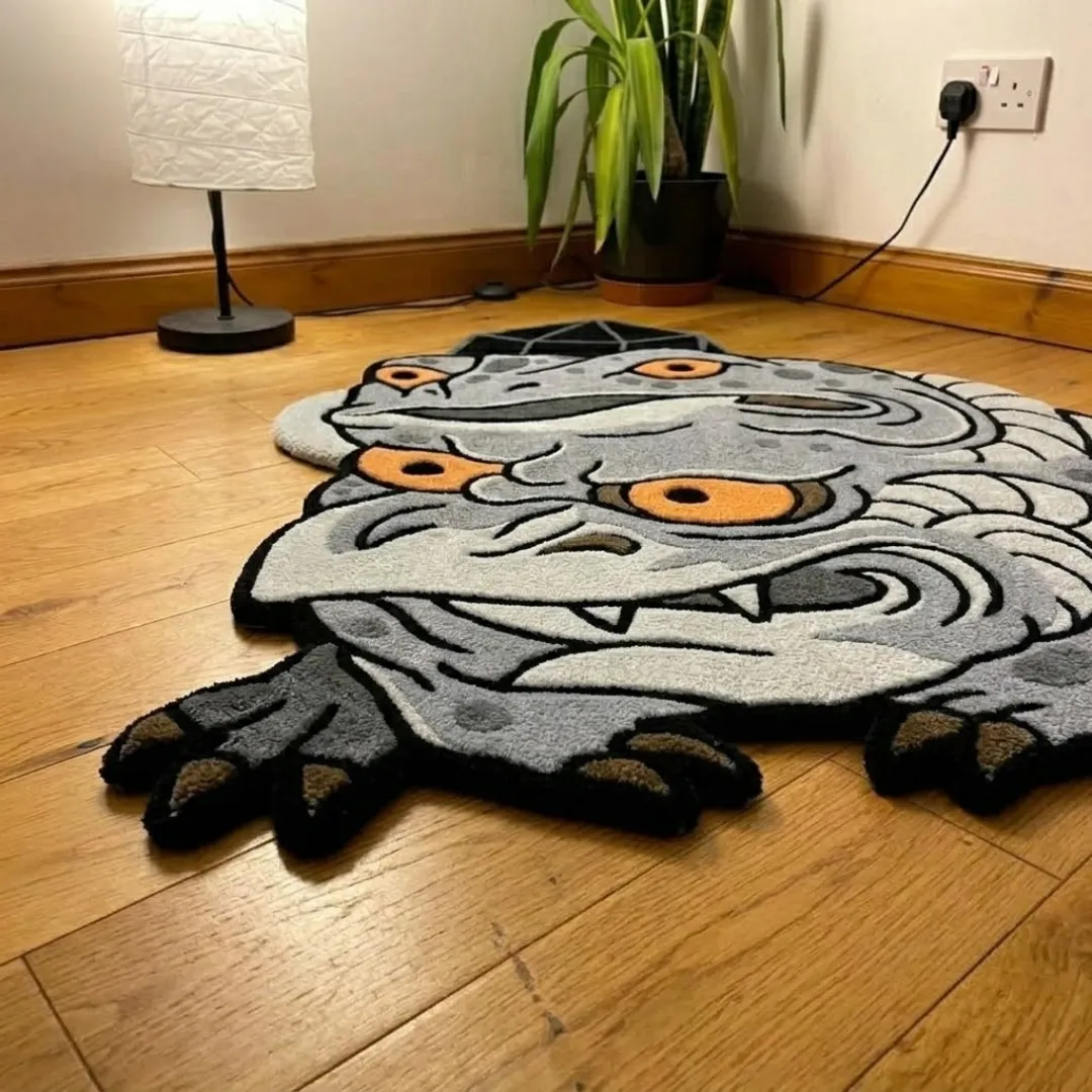 An interior lifestyle shot of a grey two-headed frog demon area rug styled on light wooden flooring in a room corner near a lamp and a potted plant.