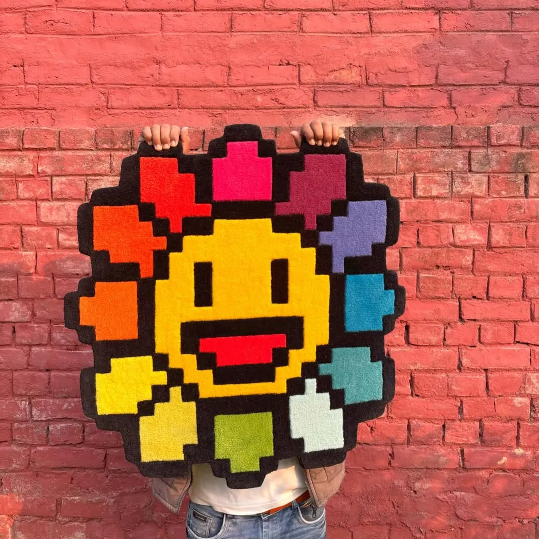 Pixelated flower-shaped rug with a smiling face, crafted from soft wool and designed to add playful energy to modern interiors.