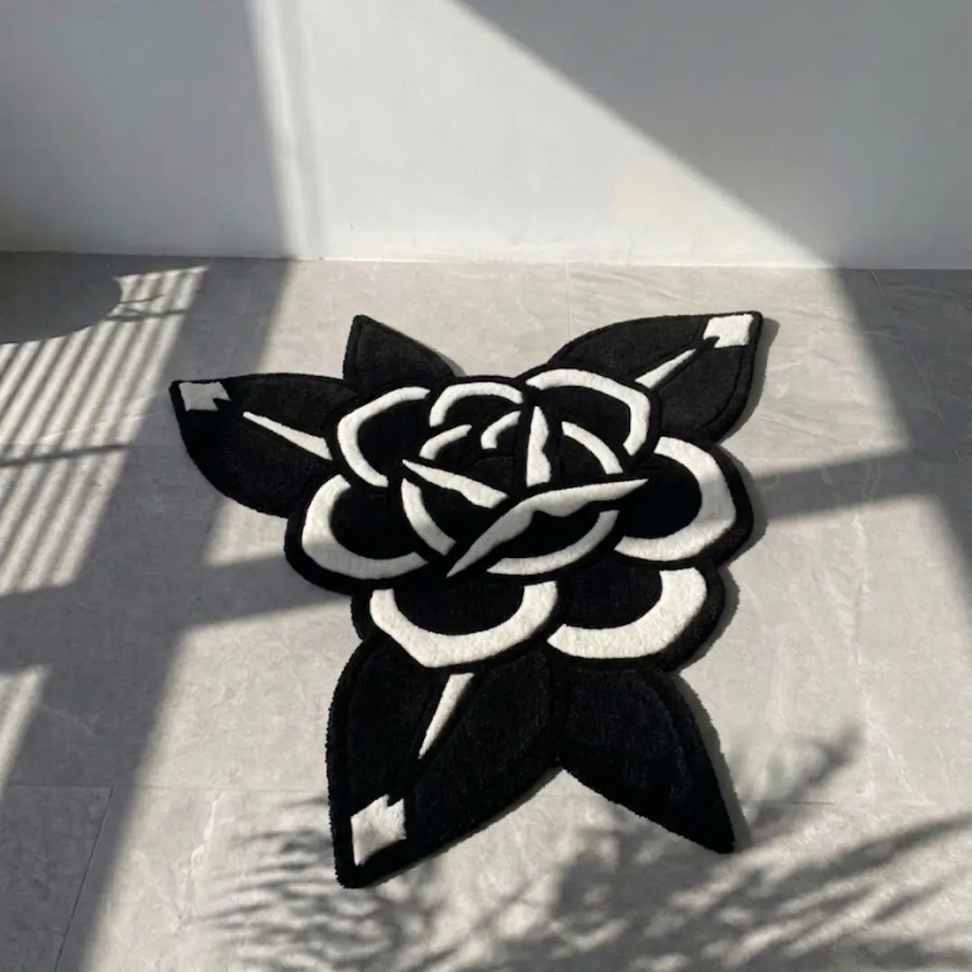 midnight bloom blackwork tattoo rug tiled floor An angled view of the Midnight Bloom Rug resting on a light grey tiled floor, beautifully illuminated by natural sunlight and striking window blind shadows. The hand-tufted custom rug features a bold blackwork tattoo-style design of a blooming rose, showcasing deep black petals defined by thick, crisp white outlines and accents.