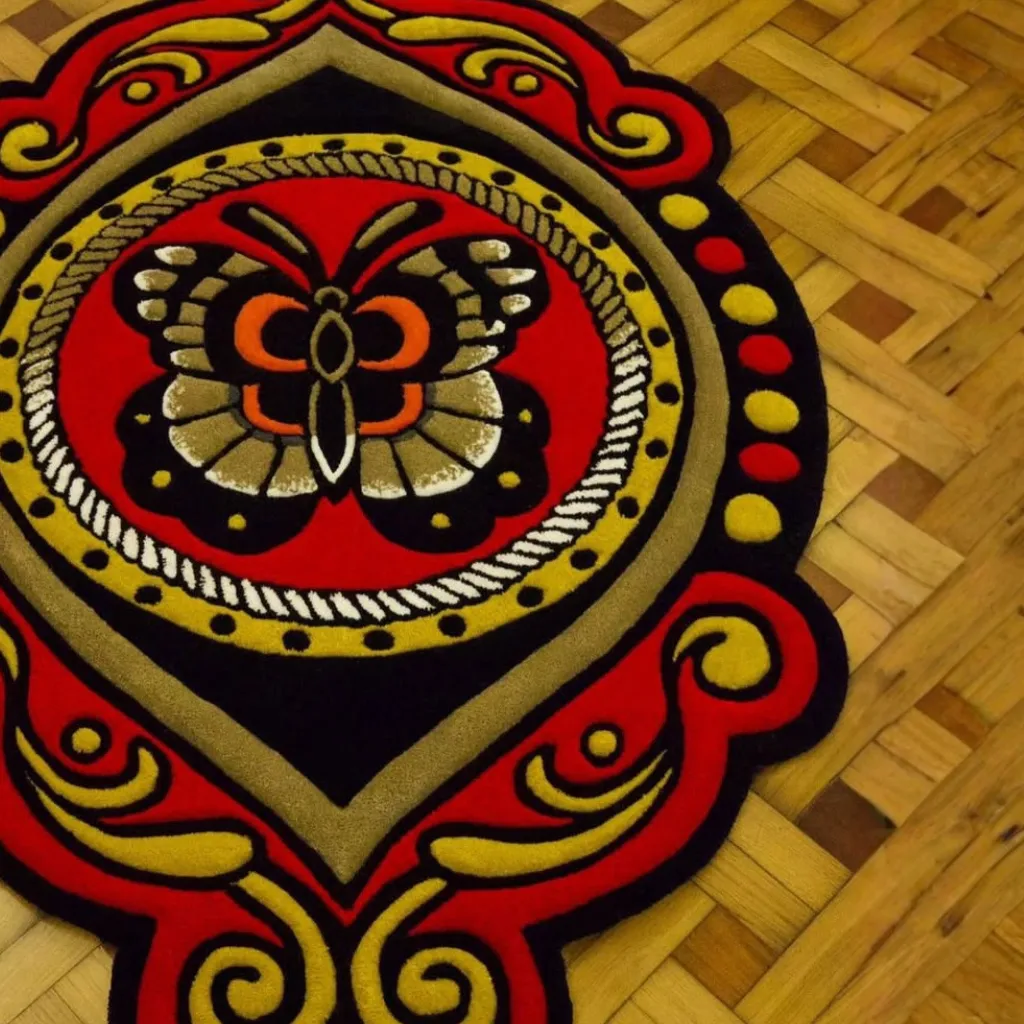 Close up texture detail of the Ember Mane rug showing the ornate red and gold scrollwork on the scalloped edge.