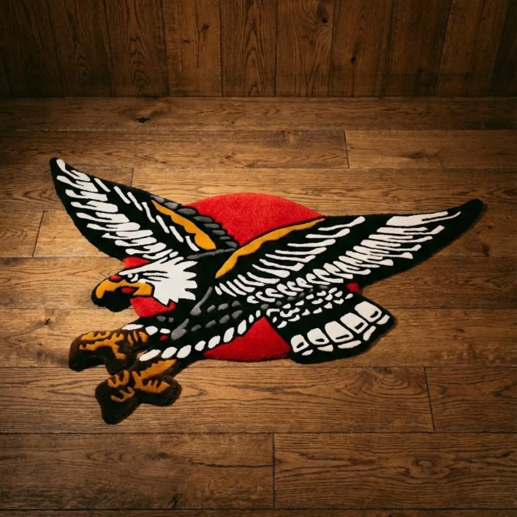 Top down view of a shaped wool rug featuring a classic American traditional tattoo design of a bald eagle in flight with a red circle background on a wooden floor.