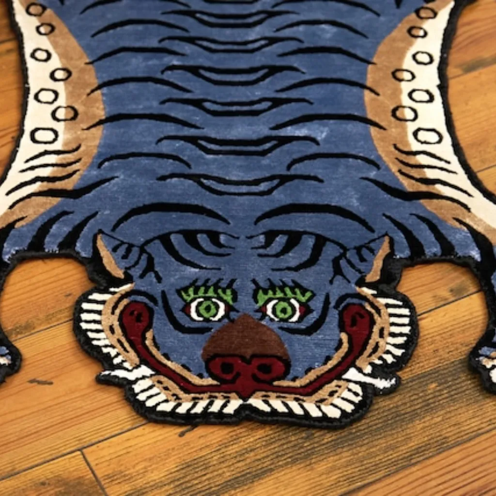 Close-up top down view of the Ashen Claw Tibetan Rug, focusing on the stylized blue-grey tiger face with striking green eyes, brown nose, and black wavy stripes.