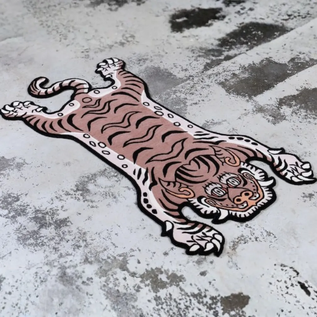 Close-up top down view of the Blush Prowl Tibetan Rug, focusing on the stylized tiger face with striking teal eyes, sharp teeth, and black wavy stripes on a soft blush pink background.