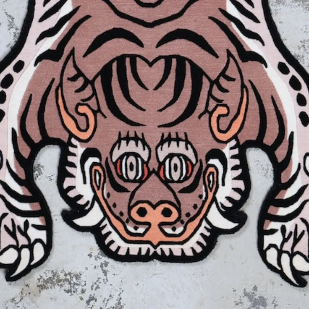 Close-up top down view of the Blush Prowl Tibetan Rug, focusing on the stylized tiger face with striking teal eyes, sharp teeth, and black wavy stripes on a soft blush pink background.