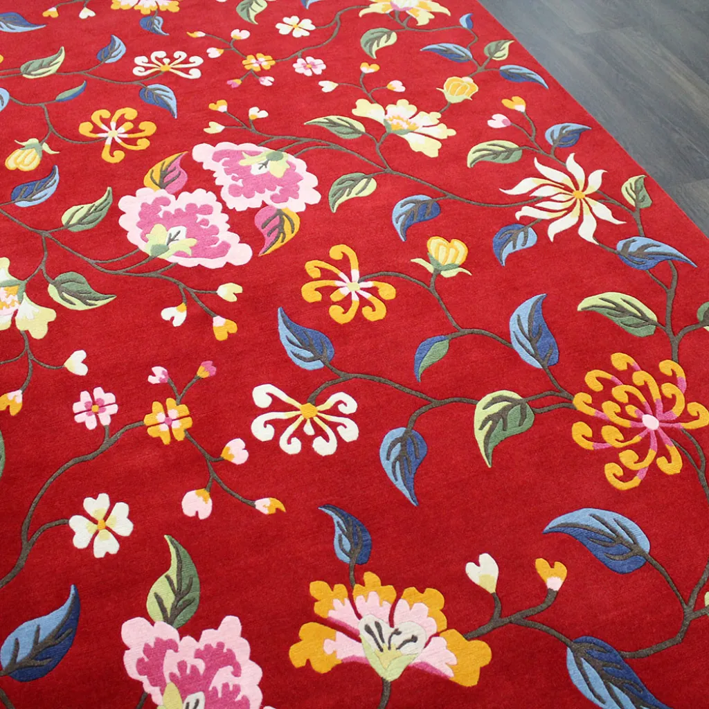 Angled close up view of the Crimson Valley rug featuring intricate trailing vines with pink, yellow, and blue flowers on a vibrant red wool background.