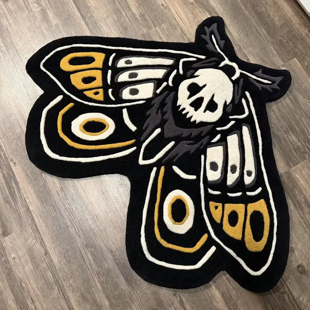 gold death moth traditional tattoo rug flat lay Top down view of the Gold Death Moth rug featuring a traditional tattoo style design with a white skull and yellow wing patterns on a black background.