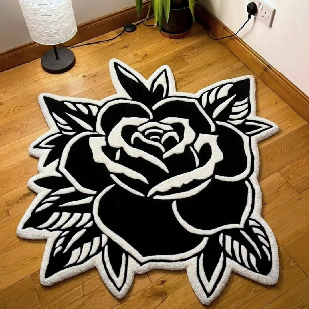 gothic black rose shaped area rug product shot A top-down view of a gothic-inspired, black-and-white rose-shaped area rug featuring traditional tattoo-style bold lines, displayed on light hardwood flooring.