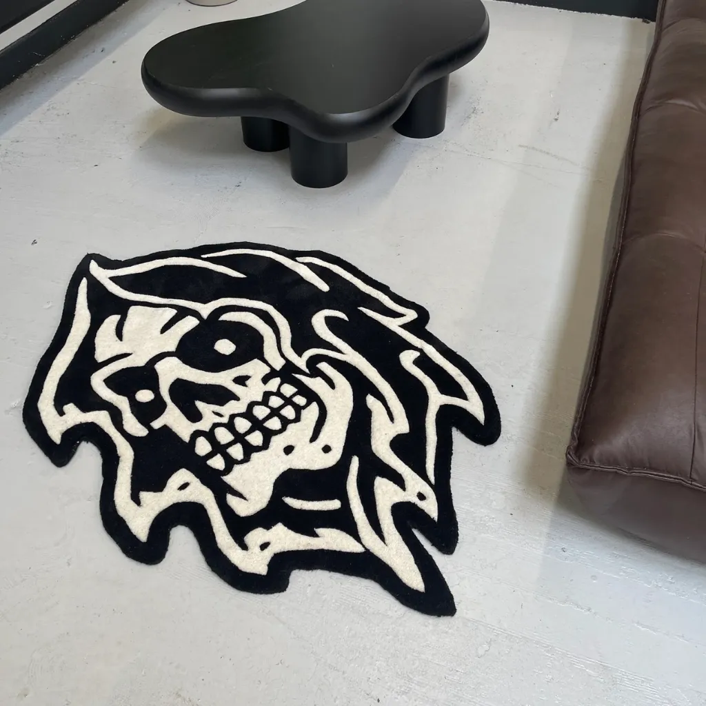 High angle view of the Grim Reaper American rug placed on a light grey floor, showing the custom die cut shape and monochromatic aesthetic next to modern furniture.