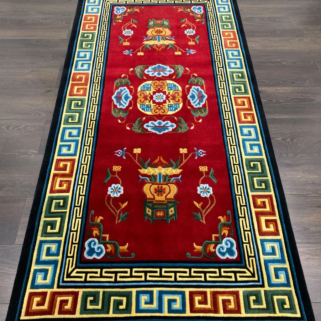 hand tufted red oriental wool rug High angle perspective of the Lotus Throne rug placed on a wooden floor, showcasing the vibrant crimson wool and the intricate multi colored border pattern suitable for a hallway or altar.
