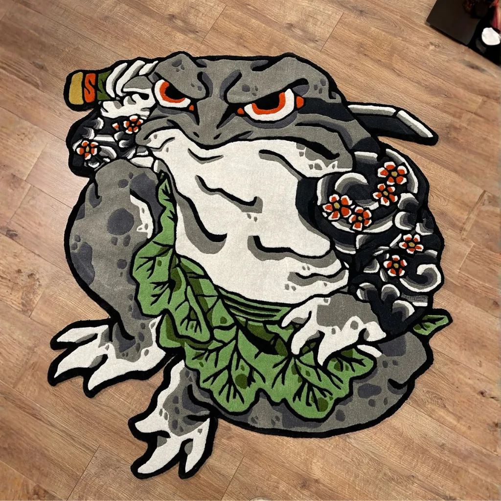 kaeru no bujin japanese warrior toad rug Top down view of the Kaeru No Bujin rug placed on a wooden floor, featuring a Japanese tattoo-style illustration of a grey warrior toad with floral arm tattoos, a katana sword, and a green leaf loincloth.