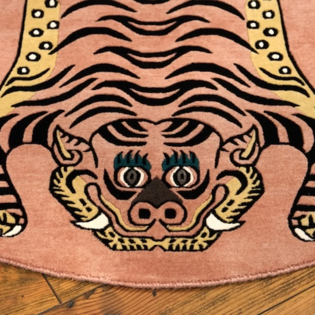 Close-up top down view of the Petal Prawl Tibetan Rug, focusing on the stylized tiger face with teal eyes, sharp teeth, and black stripes on a soft pink wool background.