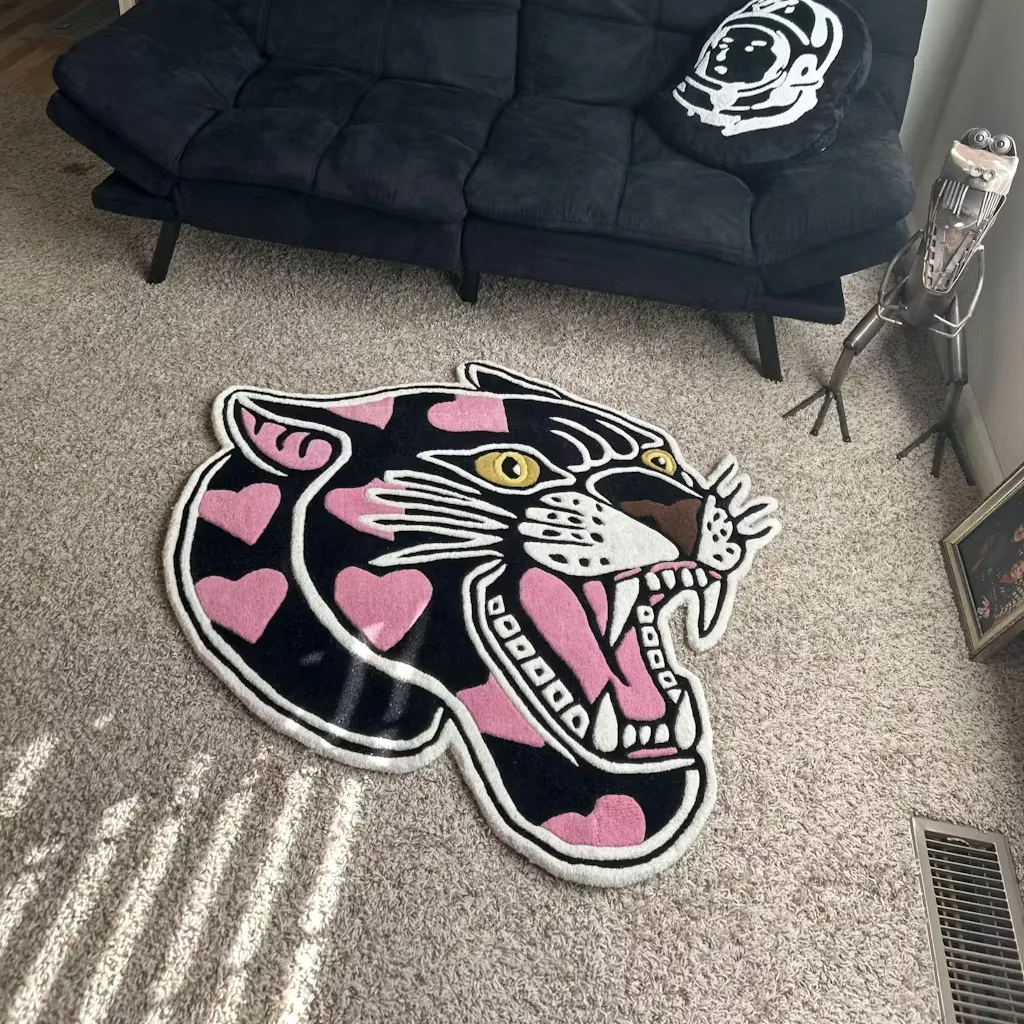 High angle view of the Pink Panther Head rug placed on a carpeted floor near a black futon, adding a bold tattoo-inspired accent to the room.