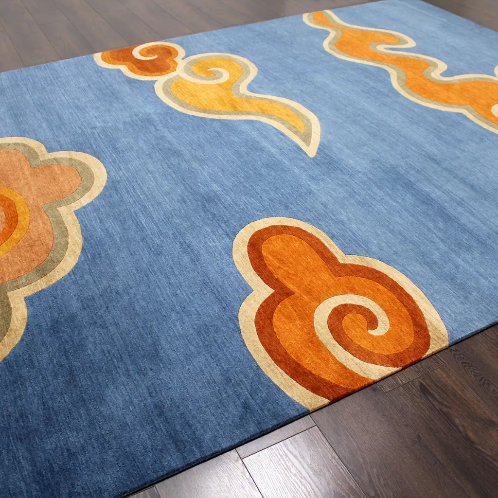 Angled perspective of the Skybound Weave rug showing the soft blue wool background and the vibrant orange and yellow traditional cloud motifs.