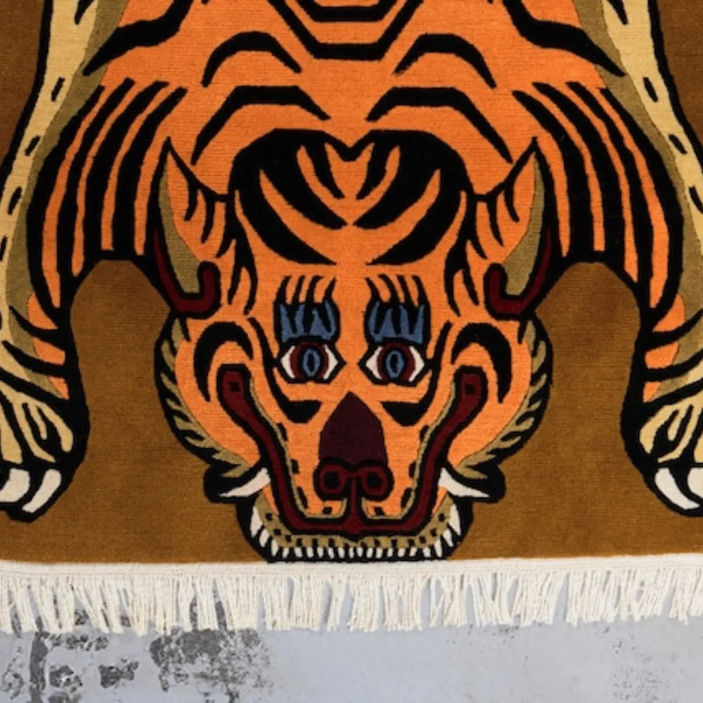 Close-up top down view of the Sunstripe Roar Tibetan Rug, focusing on the stylized tiger face with bright blue eyes, red mouth details, and black wavy stripes on a warm mustard yellow background.