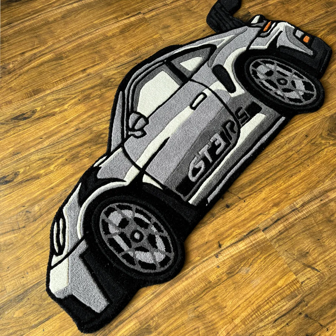 erspective view of the Apex Race rug placed on a wooden floor, highlighting the die-cut shape and the plush tufted texture of the grey high-performance car design.