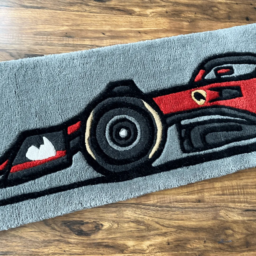 Detailed close-up of the Asphalt Aura rug showing the black rear tire and aerodynamic side panels of the red race car design.
