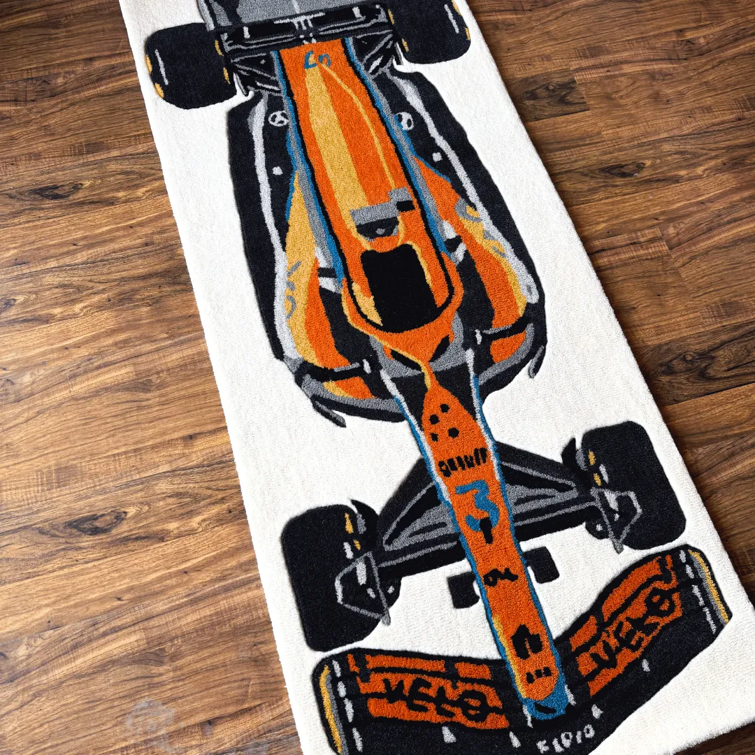 Close-up top-down detail of the Ignite Rush rug, highlighting the vibrant orange and blue livery of the race car design and the plush hand-tufted wool texture.