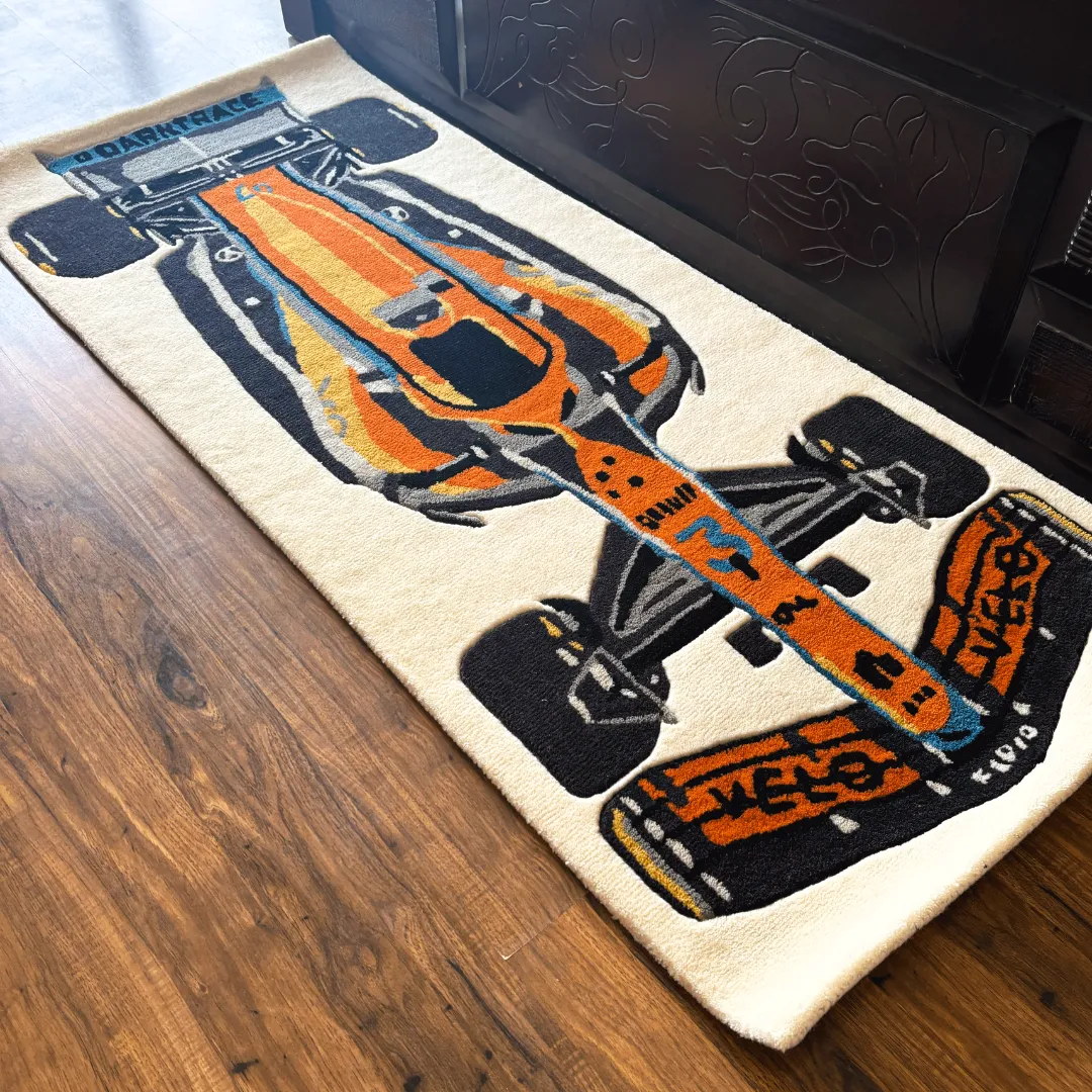 Perspective view of the Ignite Rush runner rug placed on a wooden floor, featuring a detailed tufted illustration of an orange and blue Formula 1 race car on a cream background.