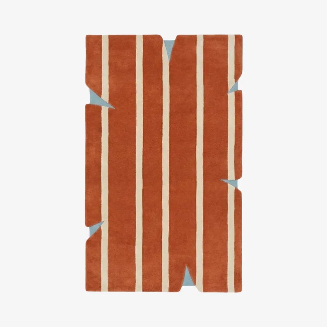 Top-down view of the Bond Break rug featuring a bold terracotta orange field with vertical cream stripes and deep triangular notches cut into the irregular silhouette, revealing light blue accents.