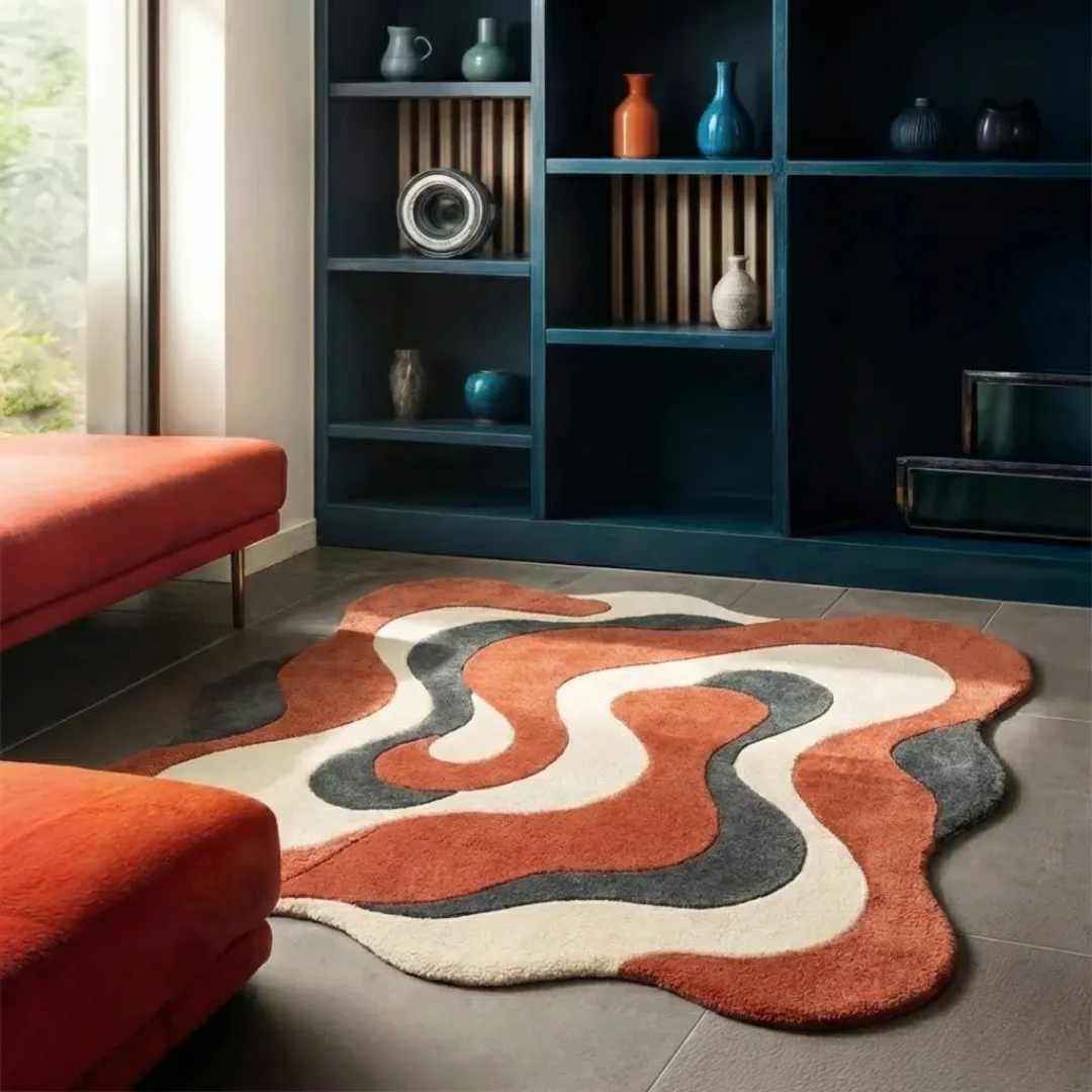 Perspective lifestyle view of the Cavaro Flow rug placed on a grey tile floor, styled next to a burnt orange velvet bench to highlight its unique wavy border and retro-inspired fluid design.