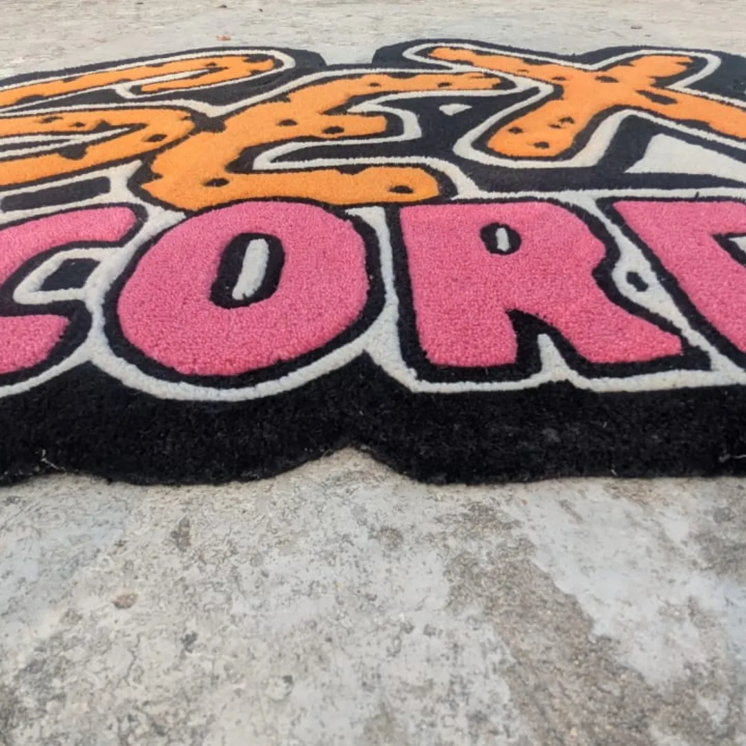Extreme close-up low-angle view of the Neon Graffiti rug on concrete, highlighting the thick, plush hand-tufted wool pile and the deep 3D carving that separates the bright pink lettering from the black base.