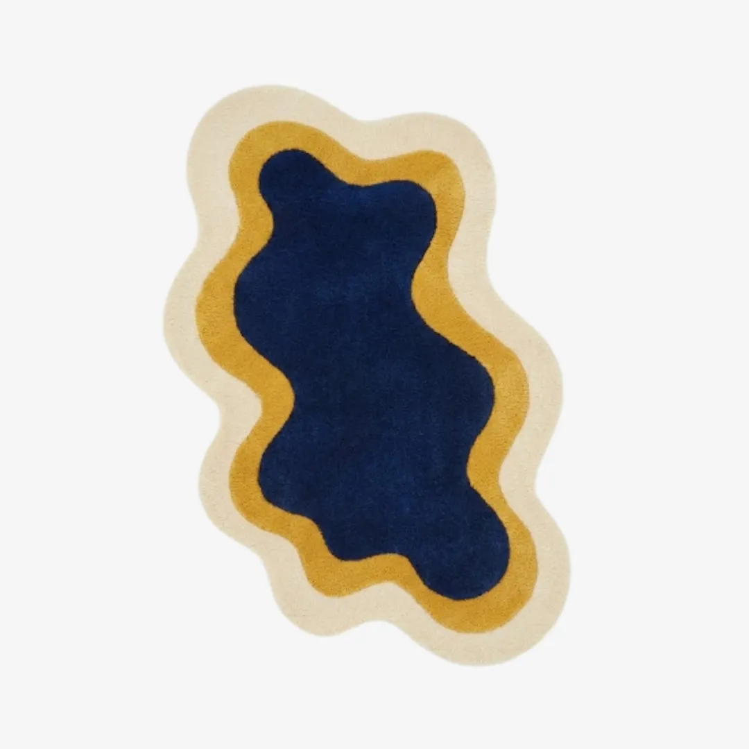 Top-down view of the Noctail Glow rug featuring a fluid, organic wavy silhouette with concentric nested layers of deep navy blue, golden yellow, and cream.