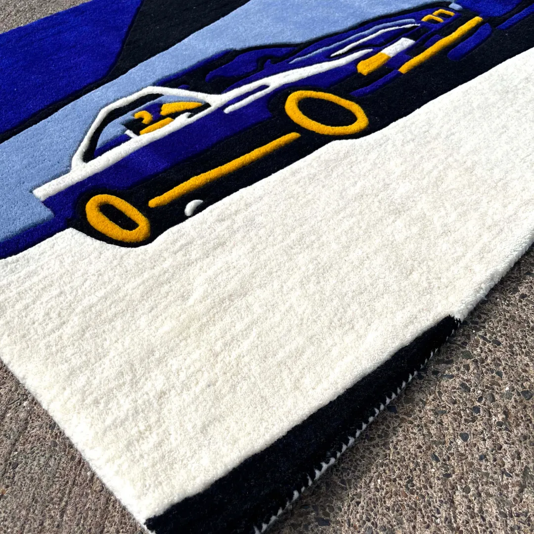 Close-up texture detail of the Noctra Veil rug, highlighting the dense, plush hand-tufted wool pile of the blue sports car design and the sharply carved yellow accents.