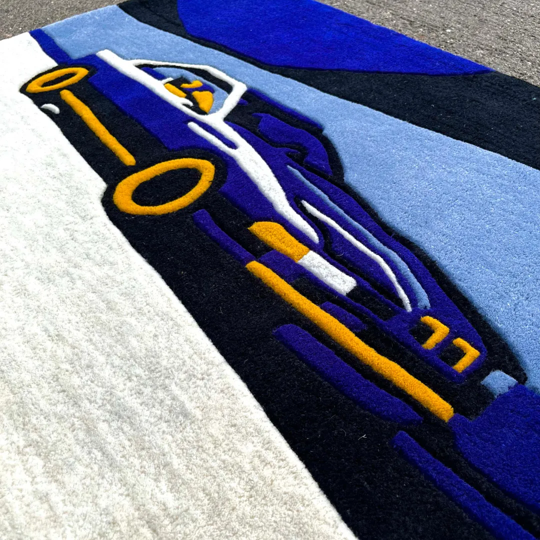 Angled close-up view of the Noctra Veil rug placed on a concrete surface, emphasizing the dense wool texture and the clean lines separating the car's bright yellow wheels from the white lower body.