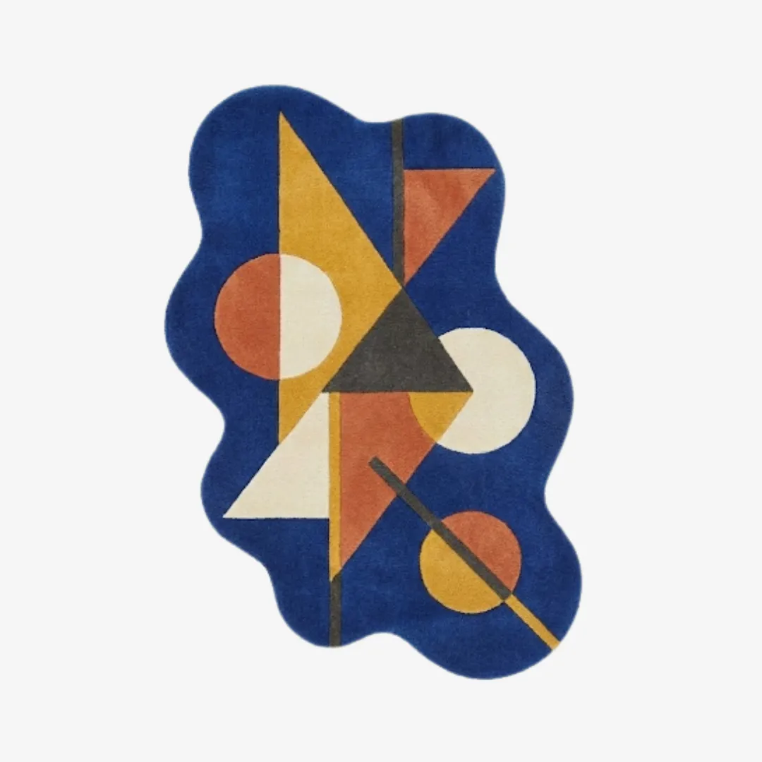 Top-down view of the Prisma Axis rug featuring a fluid, wavy silhouette and a vibrant geometric design of triangles and circles in yellow, orange, and cream on a royal blue base.