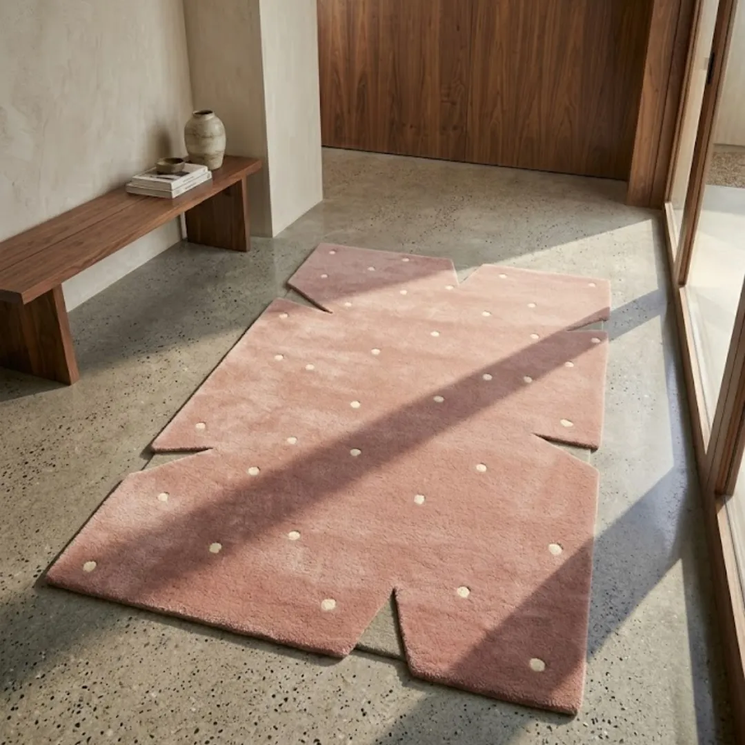 rosie stone rug lifestyle Perspective lifestyle view of the Rosie Stone rug placed on a polished concrete floor, showcasing the playful pink and cream polka dot pattern and its architectural jagged border in a sunlit room.