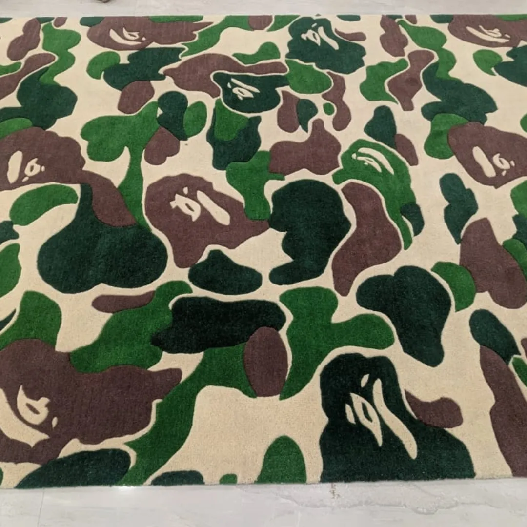 Close-up angled view of the Shadowfield Camo Terrain rug on a light tile floor, highlighting the plush hand-tufted wool texture and the sharp definition between the green, brown, and cream camouflage pattern.